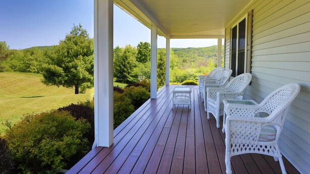 A covered porch with white wicker furniture and a view of a green landscape.