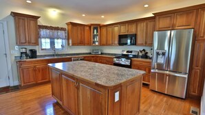 A kitchen with wooden cabinets, a granite countertop, stainless steel appliances, and a window with patterned curtains.