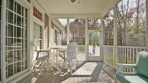 A covered porch with white furniture, including chairs and a table, and a view of the surrounding trees. - Stunning 6 bedroom 3.5 bath House in Bear Trap Dunes Community! Wifi Available, Pool, Fitness Center, Beach Shuttle, Tennis, Golf! (Ocean View)