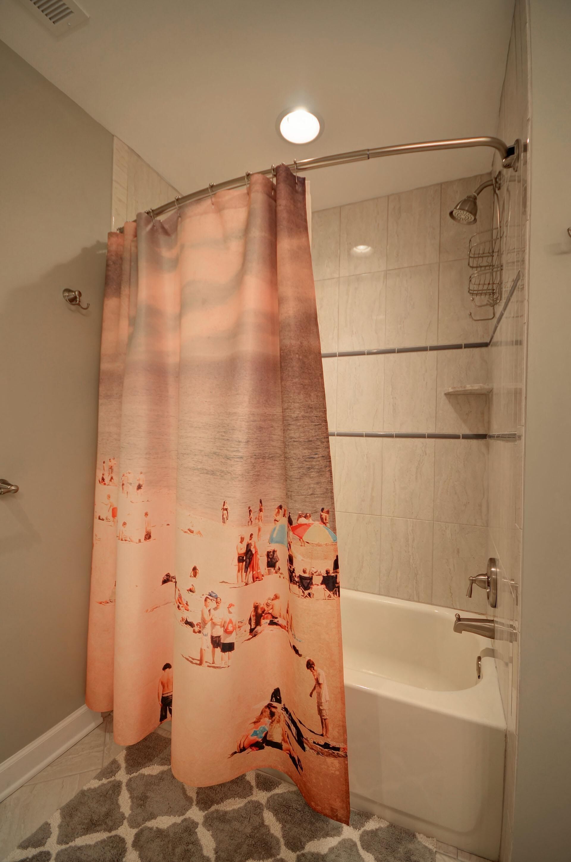 Une salle de bain avec un rideau de douche orné d’un motif de plage, une baignoire et une zone de douche carrelée.