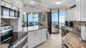 Une cuisine moderne avec des meubles blancs, des plans de travail en granit et une vue sur l’océan.