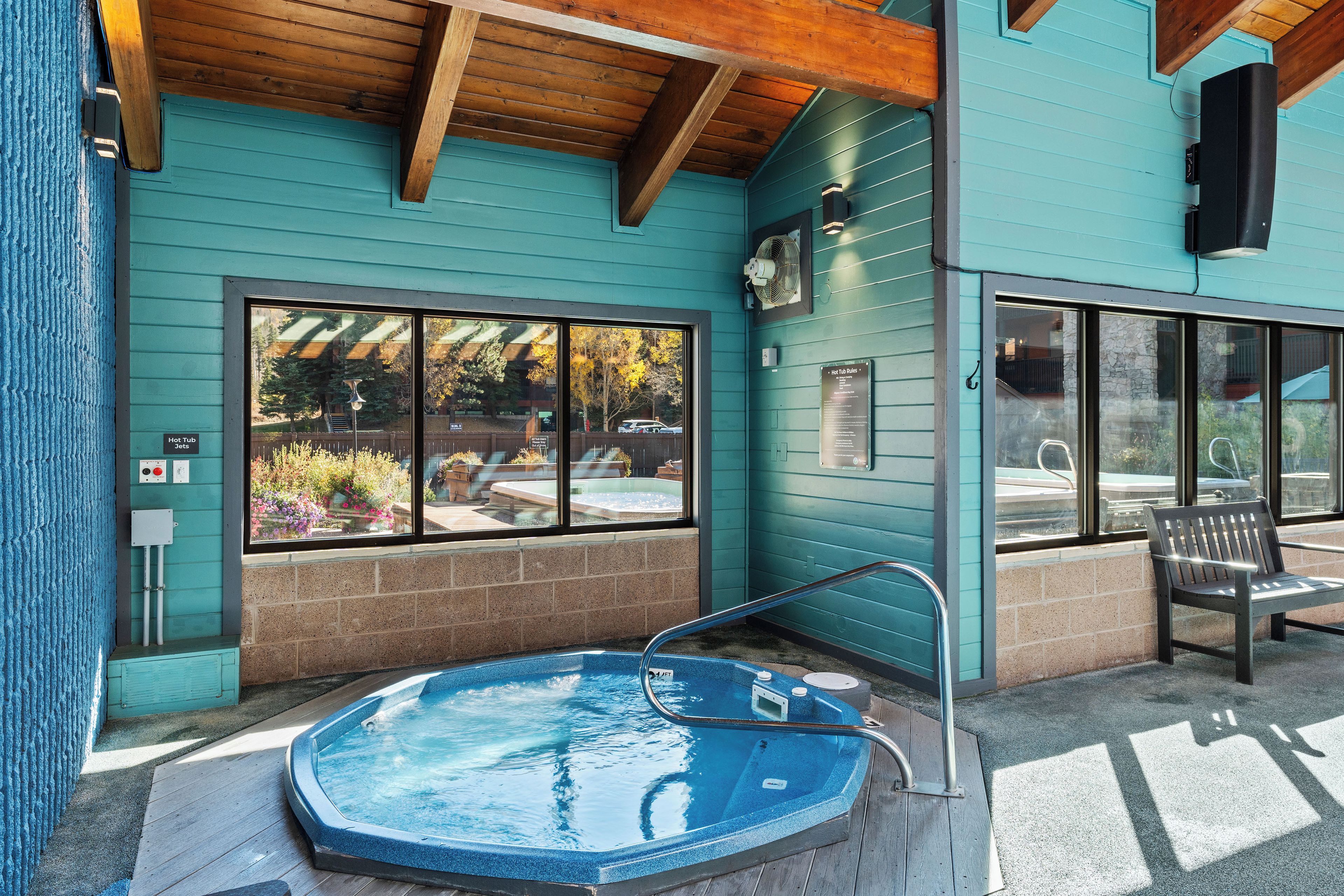 A hot tub with a wooden deck, a bench, and a window overlooking a garden.