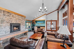 A spacious living area with a stone fireplace, leather sofas, a wooden coffee table, and a chandelier.