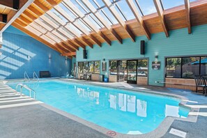 An indoor swimming pool with clear glass walls, wooden beams, and a blue exterior wall.