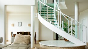 Un intérieur moderne avec un escalier en colimaçon, une plateforme ronde en marbre et un espace de vie aux lignes épurées.