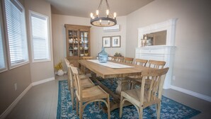 A dining room with a wooden table, chairs, a chandelier, a cabinet with dishes, and a fireplace.