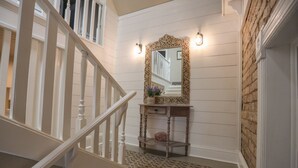 A staircase with a white railing, a wooden console table with a mirror and a plant, and a patterned rug on the floor.