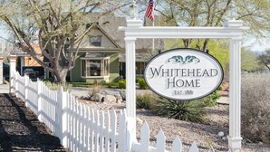 A sign for Whitehead Home with a white picket fence and a flag.