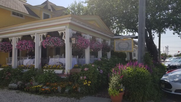 Un edificio amarillo con un porche cubierto, columnas blancas y cestas de flores colgantes.