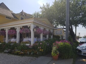 A yellow building with a covered porch, white columns, and hanging flower baskets.