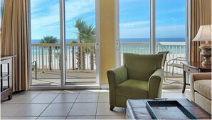 A room with a view of the beach, a green armchair, a small table, and a lamp.