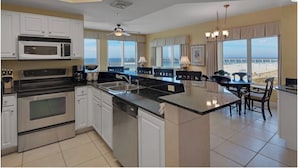 A modern kitchen with a large island, built-in appliances, and a view of the beach.