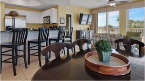 A modern kitchen with white cabinets, a dining area with a round table and chairs, a ceiling fan, and a view of the ocean.