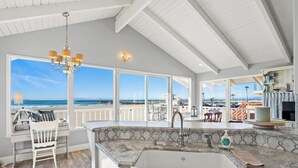 A kitchen with a large window overlooking the beach, a chandelier, and a sink with a soap dispenser. - 2405O Meet Me At the Jetty (Oxnard)