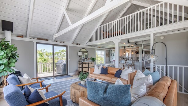 A spacious living area with a high ceiling, a wooden staircase, and a view of the outdoors. - Privacy and Views on Nantucket Island (Nantucket)