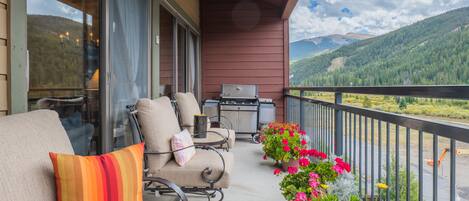 A balcony with outdoor seating, a grill, and a view of mountains.