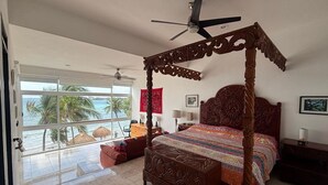 A spacious bedroom with a large bed, a ceiling fan, and a view of the ocean through large windows. - Oceanfront double size beach condo in La Sirena condominium (Akumal)