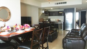 A modern living room with a dining area, a kitchen, and a ceiling fan.