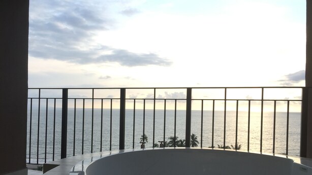 A balcony with a view of the sea, a round bathtub, and a railing.