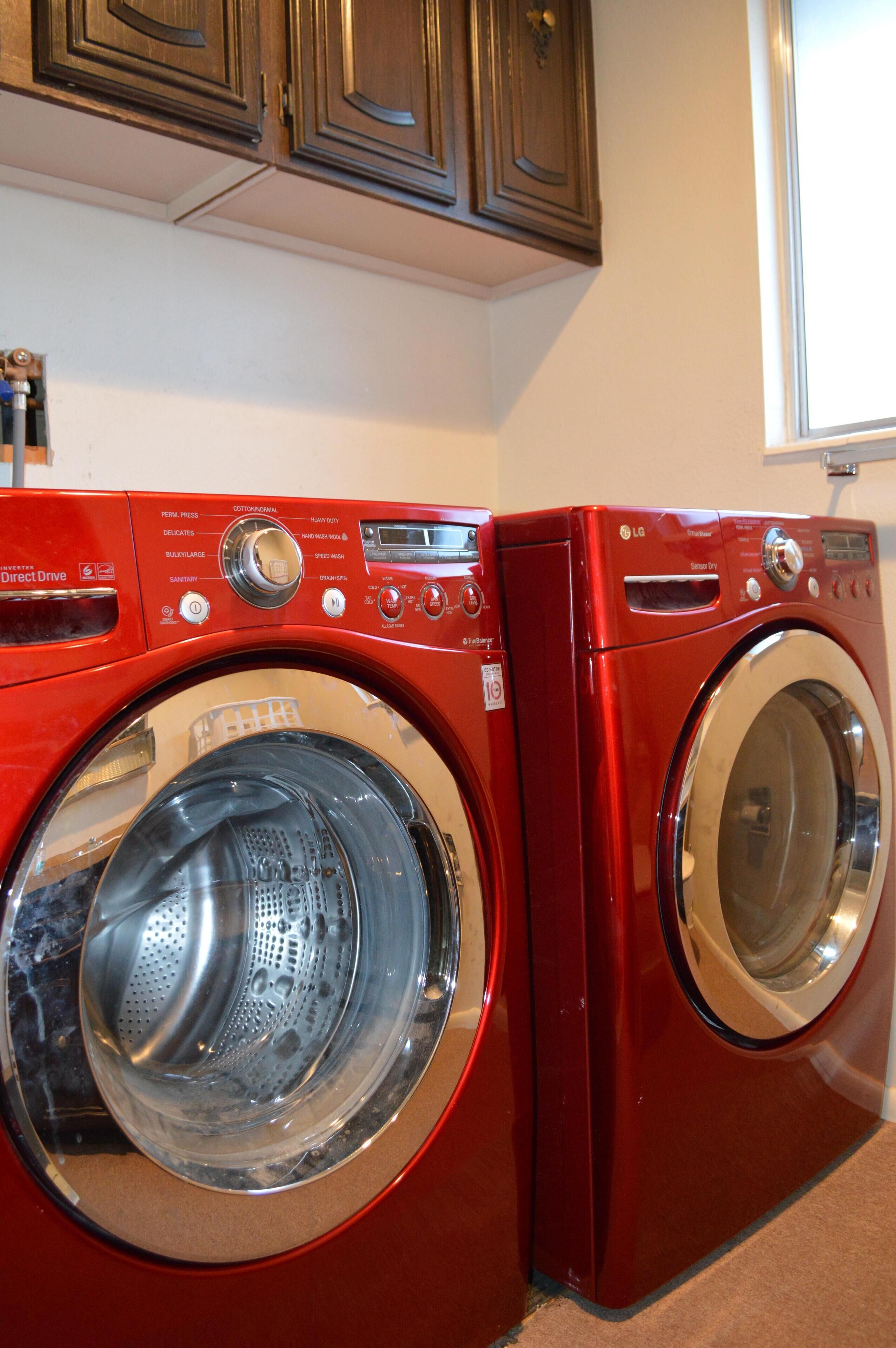 A red front-loading washing machine and dryer in a kitchen with wooden cabinets above.