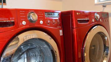 A red front-loading washing machine and dryer in a kitchen with wooden cabinets above.