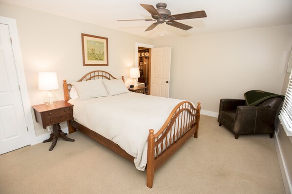 A bedroom with a wooden bed, bedside tables, a ceiling fan, a chair, and a door leading to a closet.