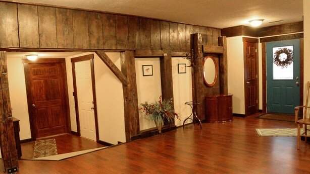 Un hall d’entrée spacieux avec un plancher en bois, une porte bleue ornée d’une guirlande et un escalier en bois.