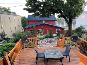 A wooden deck with a table and chairs, surrounded by a garden with various plants and a red building in the background. - The Chestnut Barn built in 1830 is nestled in the quaint Amish town of Winesburg (Winesburg)