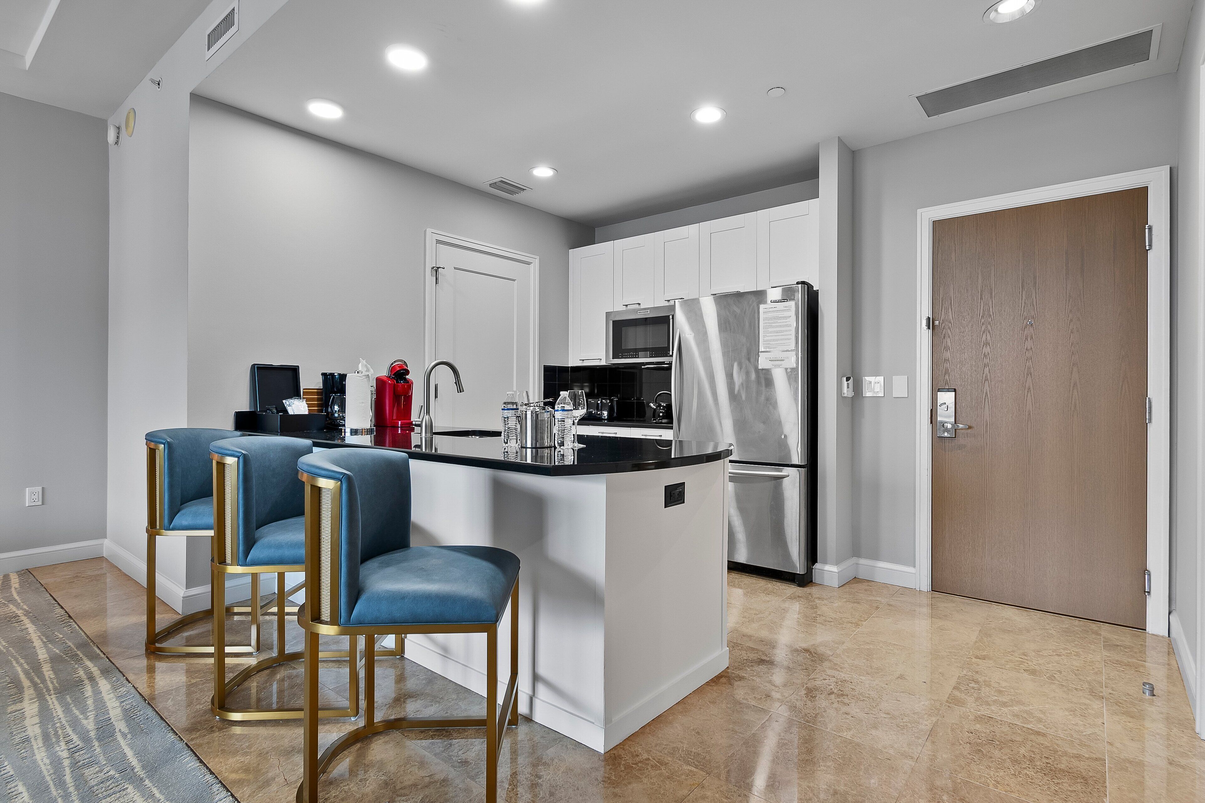 A modern kitchen with white cabinets, a stainless steel refrigerator, and a bar area with blue chairs.