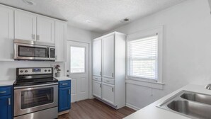 A modern kitchen with white cabinets, a stainless steel oven, a microwave, and a sink. - Relaxing 2BR Getaway Near KU Med with Pool | 18 (Kansas City)