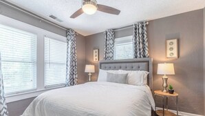 A bedroom with a large bed, two bedside tables with lamps, a ceiling fan, and patterned curtains. - Relaxing 2BR Getaway Near KU Med with Pool | 18 (Kansas City)