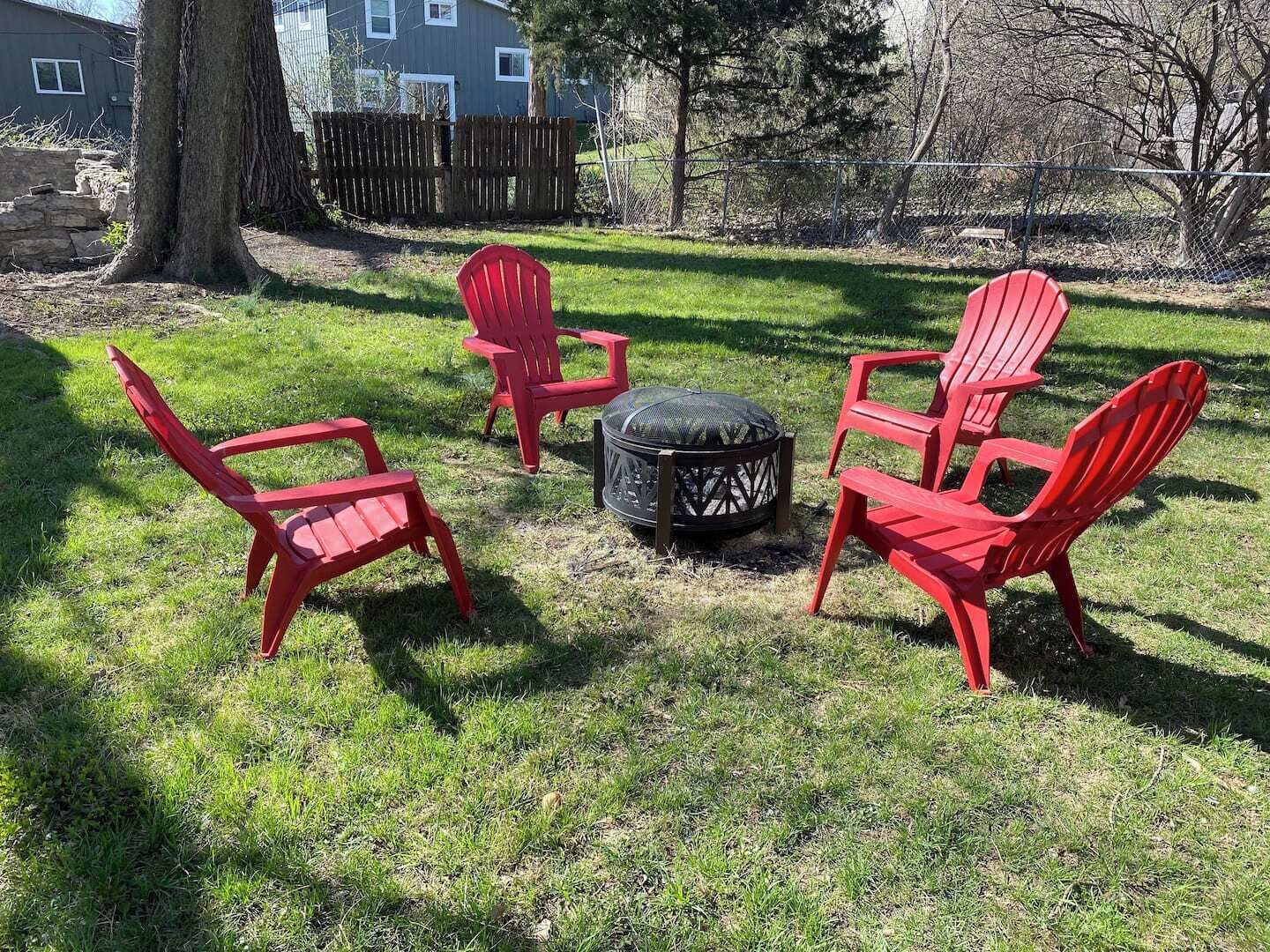 A backyard with four red Adirondack chairs arranged around a circular fire pit.