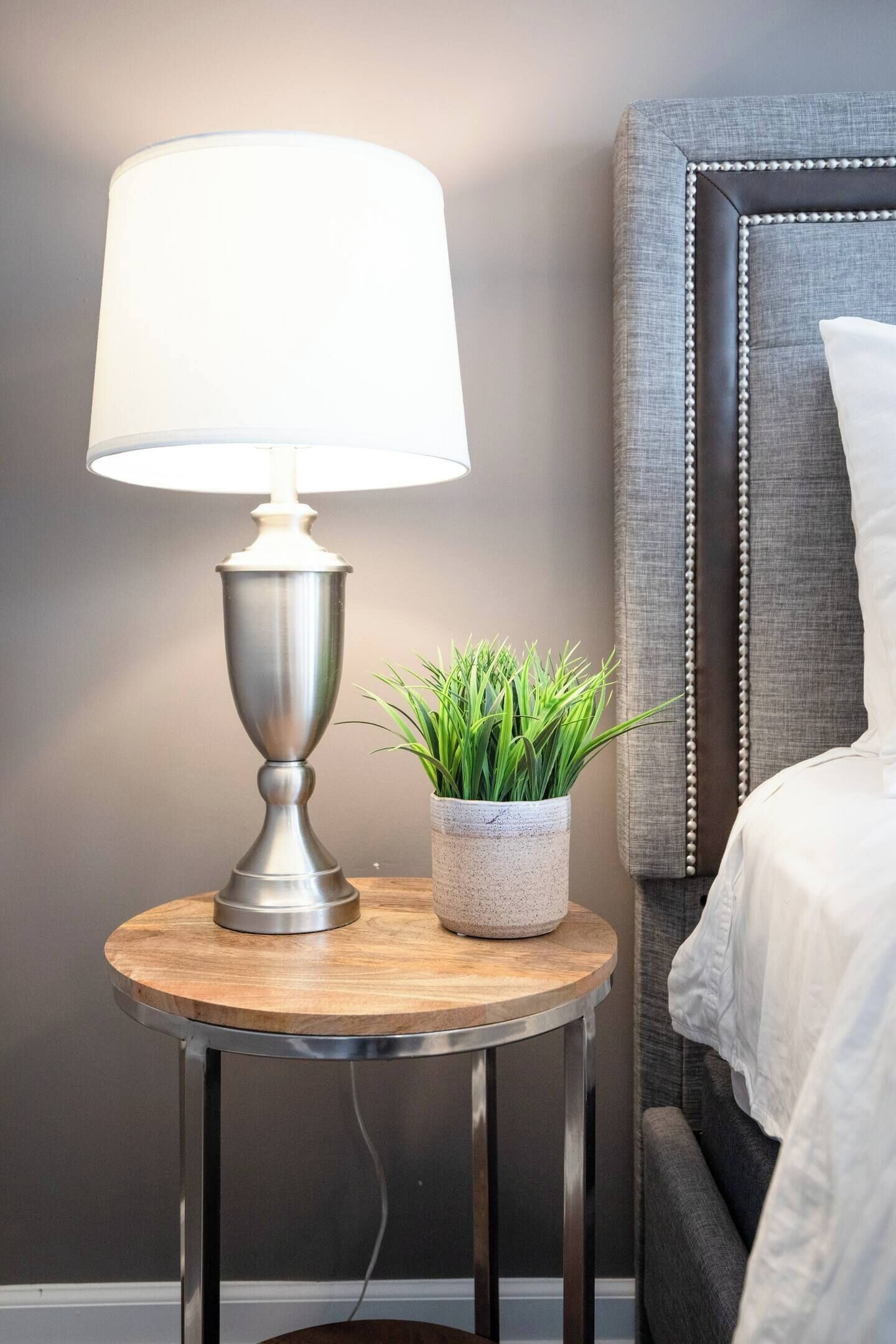 A bedside table with a lamp, a potted plant, and a bed with a headboard.