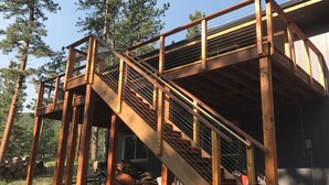 Eine Holztreppe führt zu einer Terrasse mit Geländer, umgeben von Bäumen.