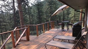 Eine Holzterrasse mit Geländer, einem Tisch mit Stühlen und einem Grill.