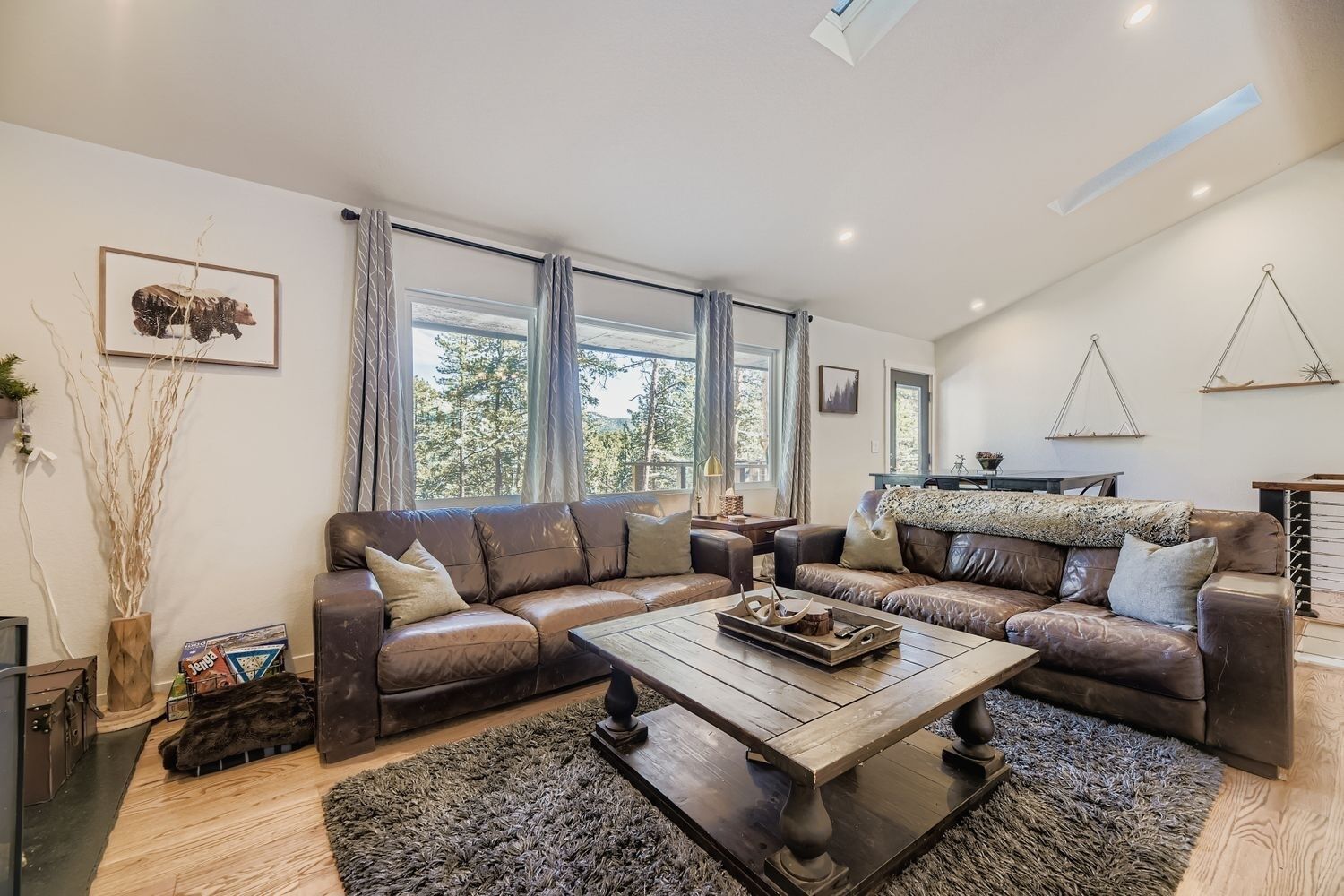 Ein modernes Wohnzimmer mit Ledersofas, einem Holztisch und großen Fenstern mit Blick auf Bäume.