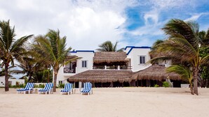 A beachfront property with a thatched-roof building, palm trees, and striped lounge chairs. - Spacious Beachside Villa with Outstanding Meals, Pool, WiFi – Large Sandy Beach (Tankah Tres)