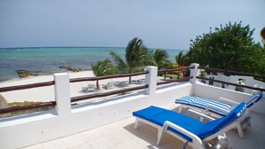 A balcony with white railings, blue cushioned lounge chairs, and a view of the ocean. - Spacious Beachside Villa with Outstanding Meals, Pool, WiFi – Large Sandy Beach (Tankah Tres)