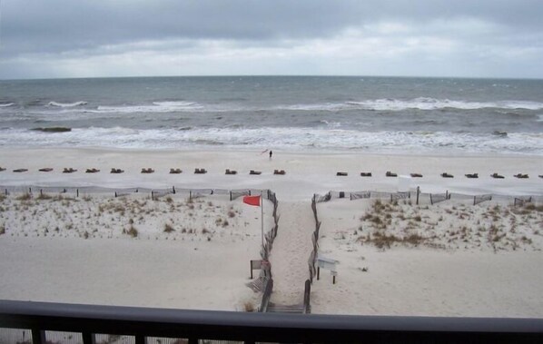 Een uitzicht op het strand met een zandpad dat naar de zee leidt, een rode vlag en een persoon die loopt.