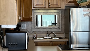 A compact kitchen with wooden cabinets, a stainless steel refrigerator, a microwave, and a sink.