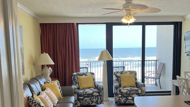 A living room with a sofa set, two armchairs, a coffee table, and a view of the ocean.