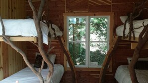 Una cabaña con literas, un ventanal con vistas a la vegetación y paredes de madera.