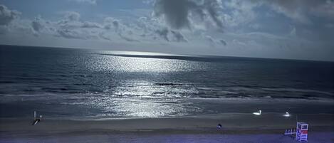 A beach with a lifeguard tower, a clear sky, and the sun reflecting on the water.
