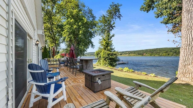 Una terraza de madera con sillas Adirondack, una chimenea y vistas a un lago.