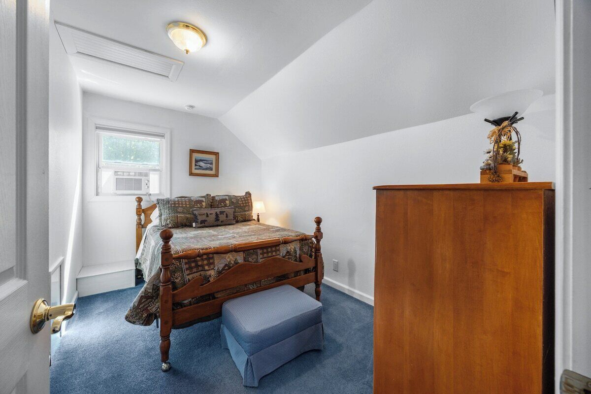 Una camera da letto con un letto di legno, un tappeto blu, un comò in legno e una finestra con condizionatore.