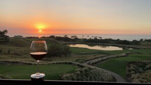 A sunset view from a balcony with a glass of red wine, overlooking a golf course with water features and trees. - Uninterrupted Sunset, Ocean and Golf Course Views from our Lanai and Interior (Kamuela)