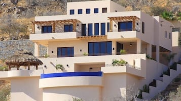 A multi-story building with balconies, a thatched-roof structure, and a blue railing.