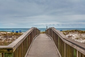 A wooden boardwalk leading to the beach with beach umbrellas and sand dunes.