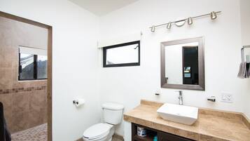 Une salle de bain équipée de toilettes, d’un lavabo, d’un miroir et d’un porte-serviettes.