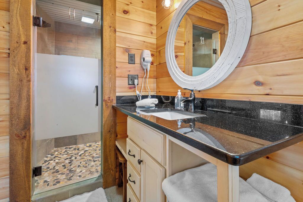 A bathroom with a glass shower enclosure, a sink with a black countertop, and wooden walls.